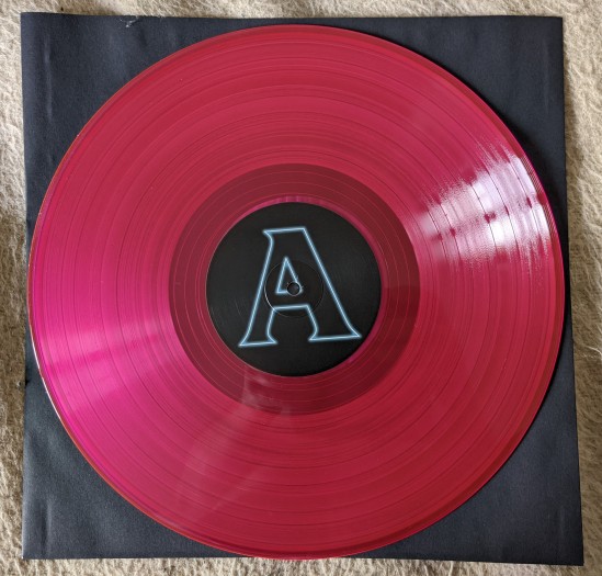 Eine durchscheinend-magenta farbene Vinyl-Langspielplatte auf schwarzer Schutzhülle.