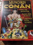 Titelbild des Spiels "Munchkin - Conan" Ein gezeichneter Barbar mit blutigem Schwert steht auf einem Goldhaufen. Daneben steht "TÖTE DIE MONSTER
- KLAU DEN SCHATZ -
ERSTICH DEINE KUMPEL"