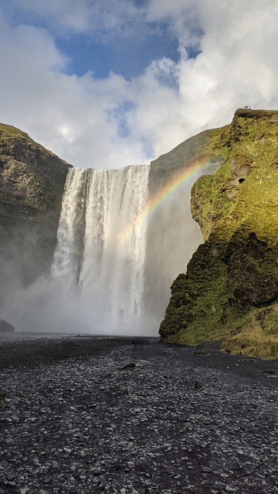 Der Wasserfall Skógafoss mit Regenbogen und ohne Leute auf den Steinen davor